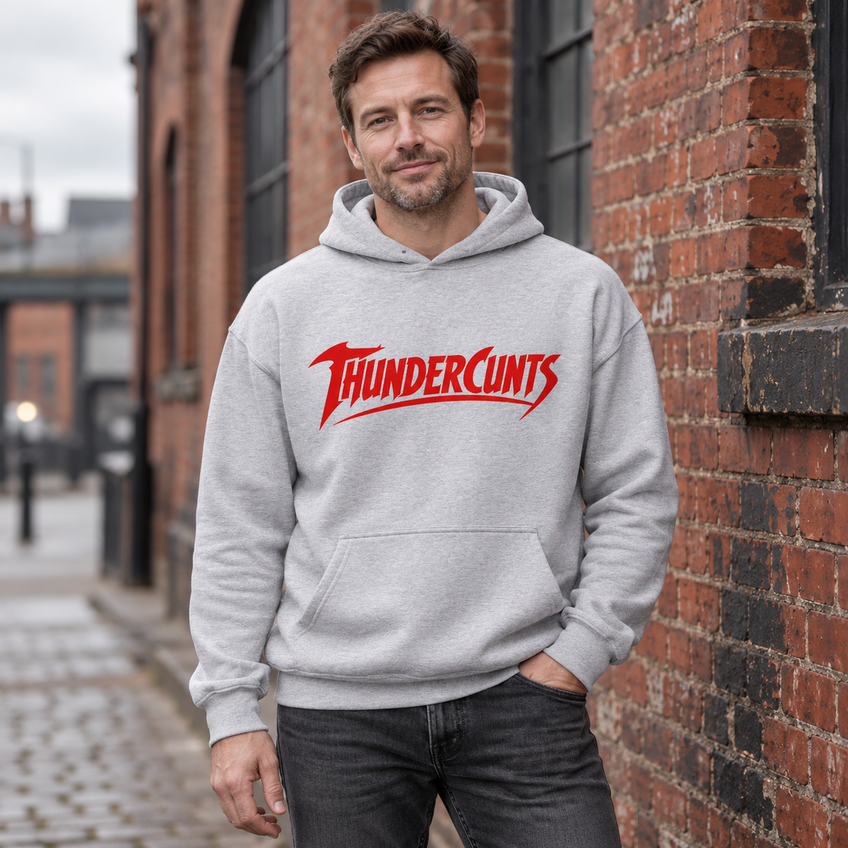 Man wearing a sport grey Thundercunts hoodie with red chest lettering outside a brick warehouse.