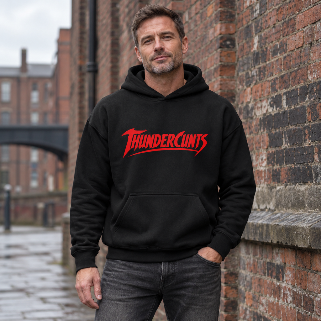 Man modelling a black Thundercunts hoodie with red lettering beside a brick wall.
